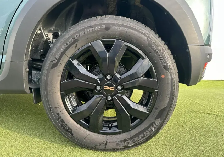 Gros plan sur la roue arrière droite avec jante aluminium noire brillante du Dacia Sandero Stepway Vert Cèdre.