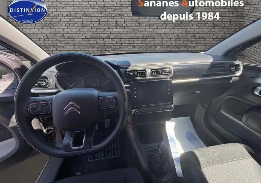 Vue intérieure avant centrée sur le volant et la console centrale d'une Citroën C3 2022 avec sellerie tissu gris.