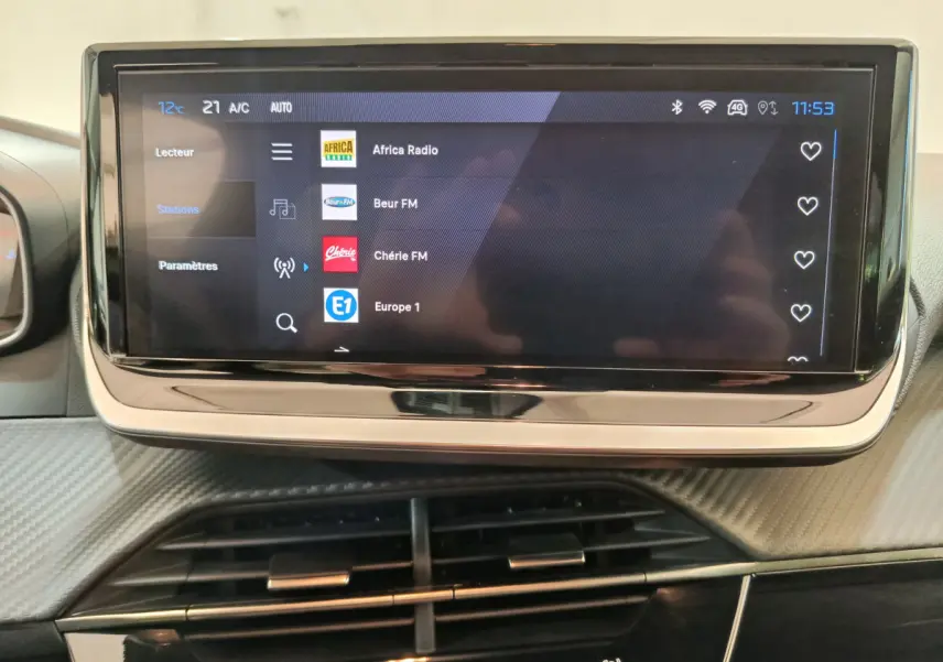 Écran tactile central affichant les stations radio dans l'habitacle d'une Peugeot 208 gris clair, vue de face.