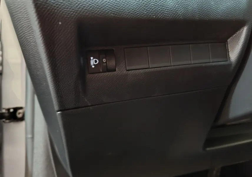Gros plan sur le tableau de bord côté gauche de la Peugeot 208 gris clair, avec molette de réglage des phares.