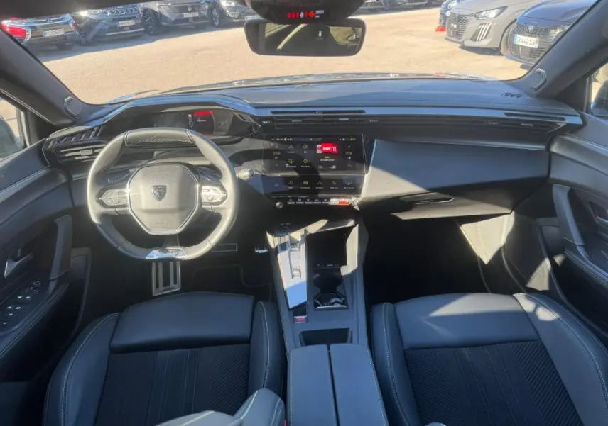 Vue intérieure avant de la Peugeot 408 Hybrid gris, avec volant cuir compact, cockpit numérique et console centrale moderne.