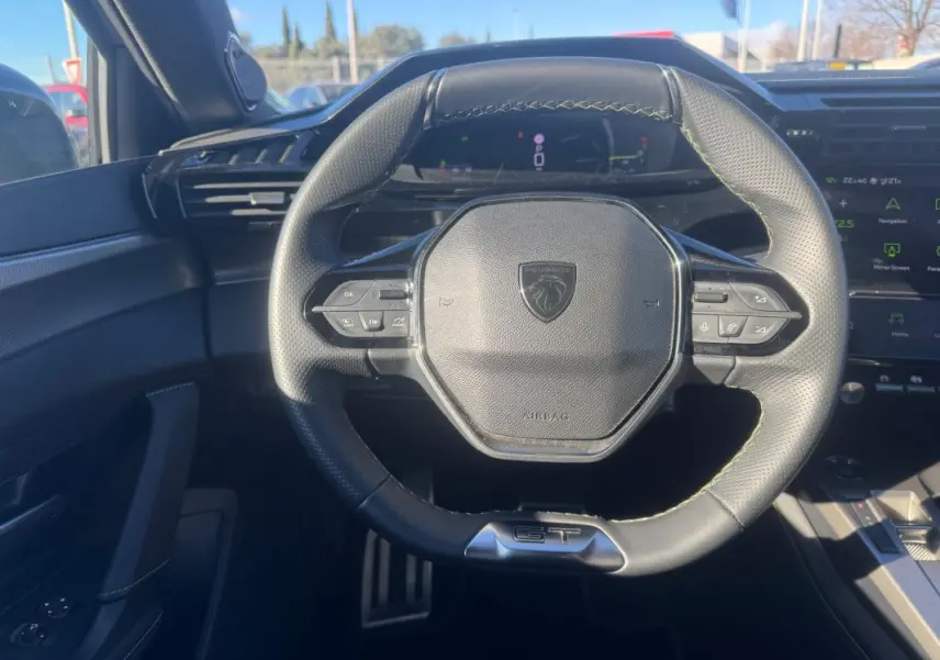 Vue rapprochée du volant cuir noir GT de la Peugeot 408 Hybrid 2024 avec commandes intégrées et cockpit numérique en arrière-plan.