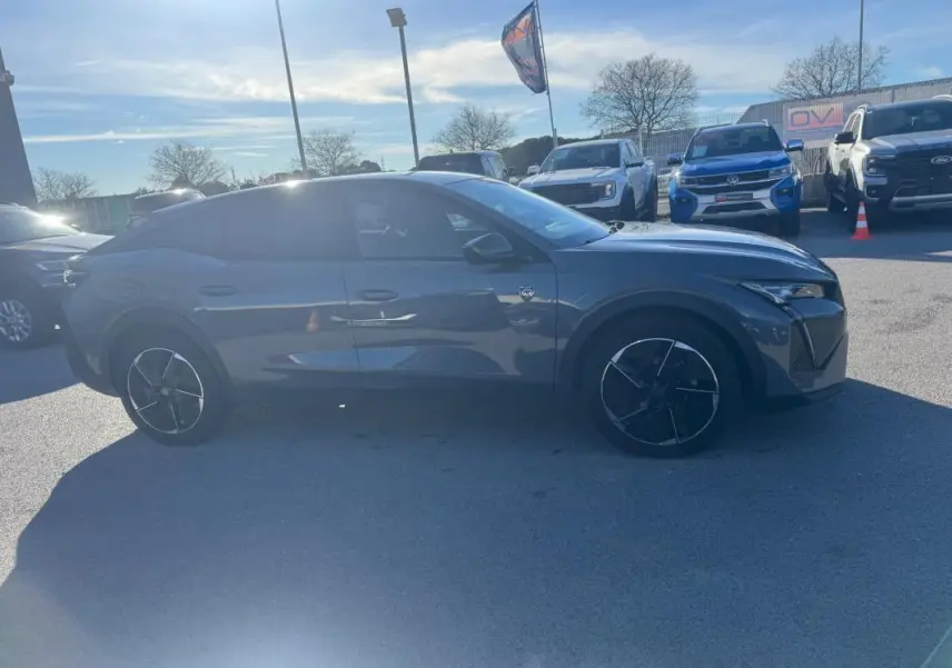 Peugeot 408 gris vue de profil côté droit, avec jantes alliage noires et vitres teintées, stationnée en extérieur.