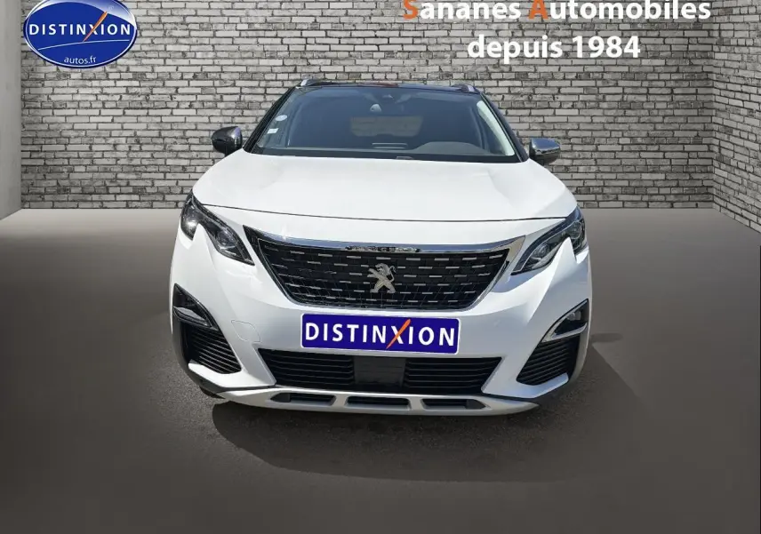 Vue avant d'un Peugeot 3008 blanc nacré avec calandre noire et logo lion au centre, sur fond de mur en briques grises.