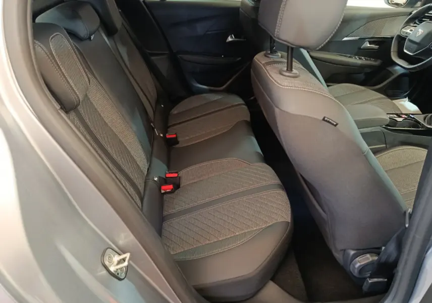 Vue intérieure côté arrière droit de la Peugeot 208 gris clair, montrant les sièges tissu et cuir avec surpiqûres contrastées.