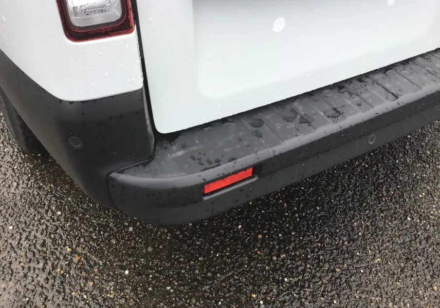 Gros plan sur le pare-chocs arrière noir et la partie blanche de la porte du Renault Trafic Fourgon L2H1 2023 sous la pluie.