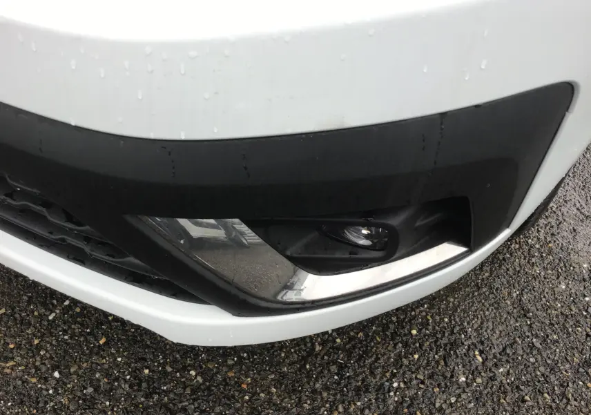 Gros plan sur le pare-chocs avant blanc du Renault Trafic Fourgon 2023, mettant en valeur le feu antibrouillard et la grille noire.