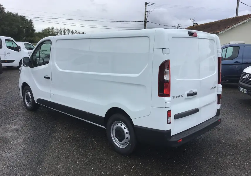 Renault Trafic Fourgon blanc en vue 3/4 arrière droit, avec caméra de recul et feux arrière verticaux visibles.