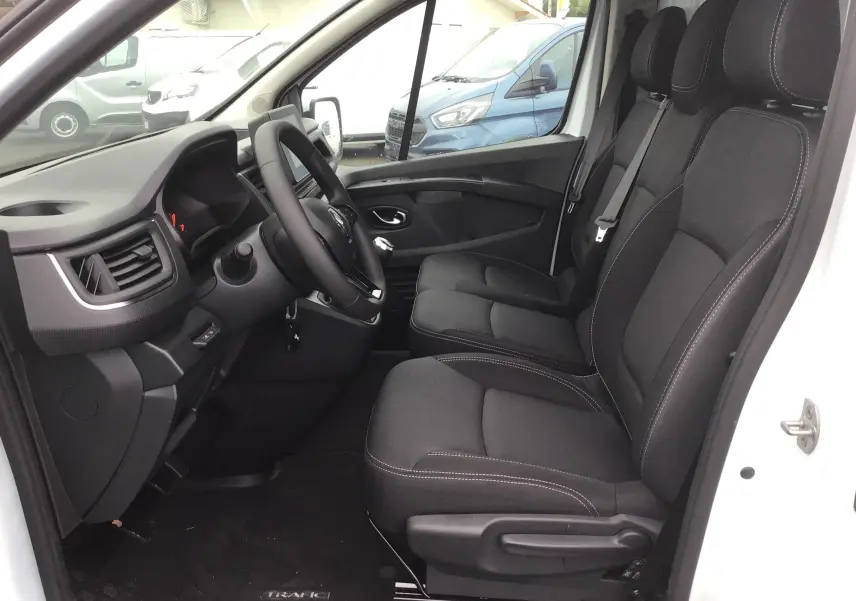 Intérieur côté conducteur du Renault Trafic Fourgon blanc 2023, sièges noirs et tableau de bord moderne visible.