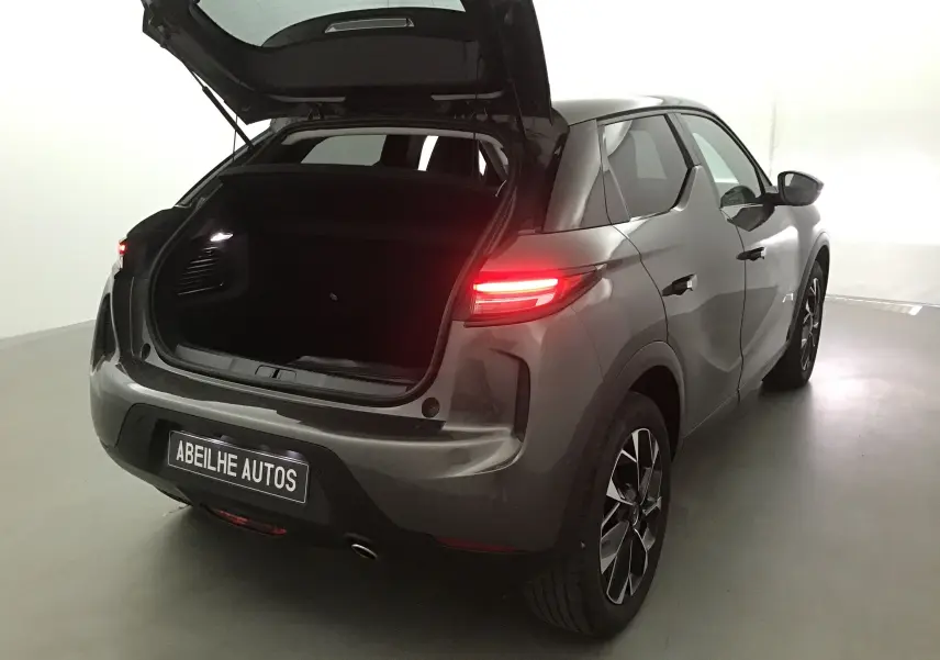 Vue 3/4 arrière droite du DS3 Crossback gris platinium 2024 avec coffre ouvert et feux arrière allumés.