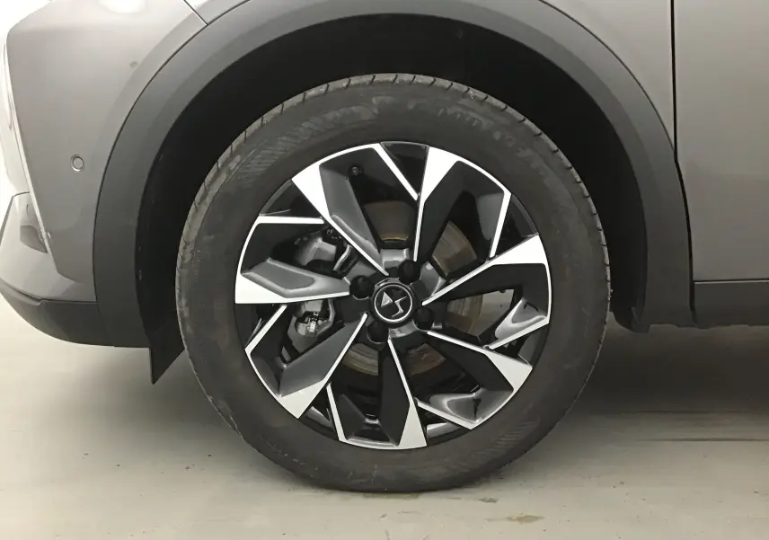 Gros plan sur la roue avant gauche du DS3 Crossback gris platinium, mettant en valeur la jante noire et argentée au design moderne.