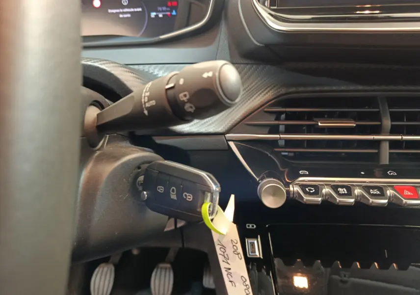 Gros plan sur le tableau de bord et la clé insérée côté gauche d'une Peugeot 208 gris clair 2025 PureTech Allure