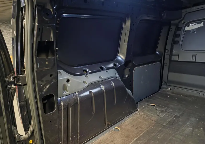 Vue intérieure du compartiment de charge noir du Volkswagen Caddy Cargo 2024, montrant les parois métalliques et le plancher.