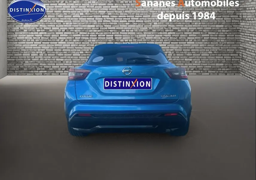Vue arrière d'un Nissan Juke bleu clair 2020, avec logo et feux arrière distinctifs, dans un studio avec mur en briques.