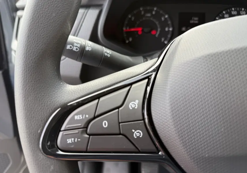 Gros plan sur les commandes de régulateur de vitesse au volant gris du Renault Trafic Combi 2025, tableau de bord en arrière-plan.