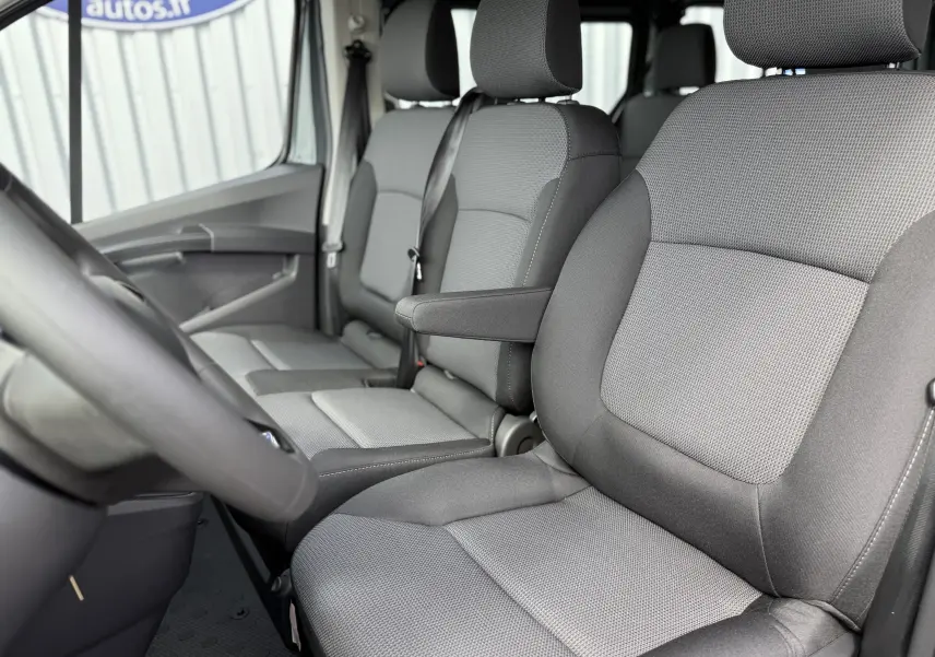 Vue intérieure côté conducteur du Renault Trafic Combi 2025, sièges tissu gris avec accoudoir central.