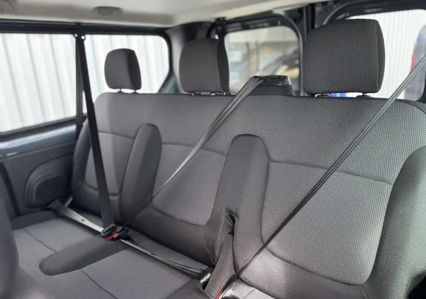 Vue intérieure sur la banquette arrière en tissu gris du Renault Trafic Combi 2025, avec ceintures de sécurité attachées.