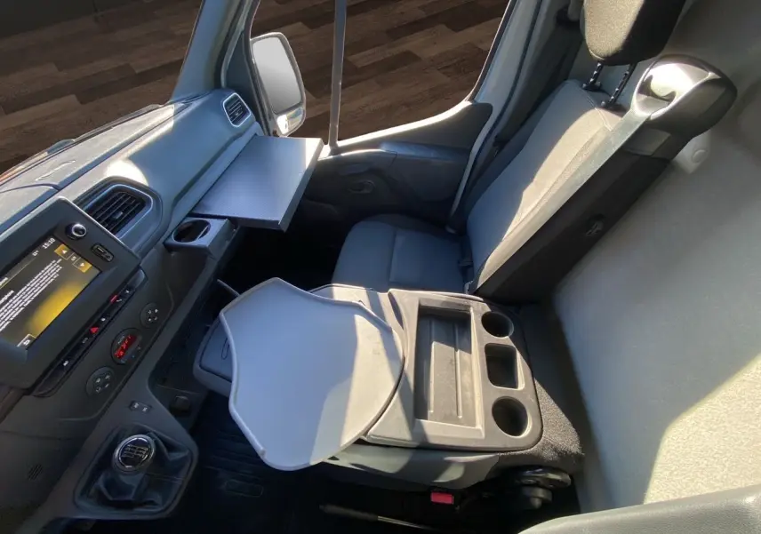 Vue intérieure côté passager du Nissan Interstar blanc 2022, montrant le siège, la console avec porte-gobelets et tablette rabattable.