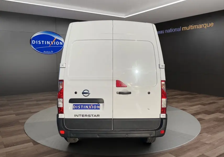 Vue arrière d’un utilitaire blanc Nissan Interstar avec portes battantes et logo visible en intérieur showroom.