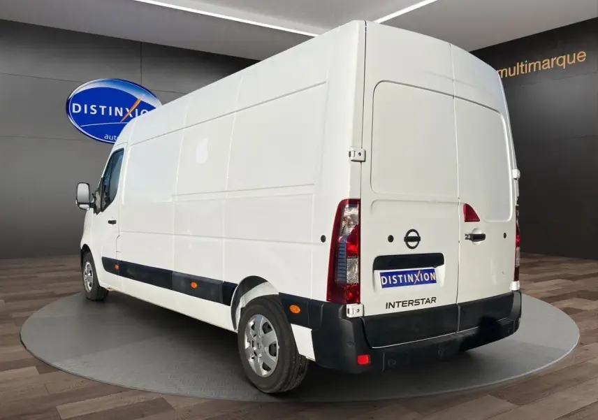 Vue 3/4 arrière droite d’un utilitaire Nissan Interstar blanc avec bande noire latérale et feux arrière verticaux.