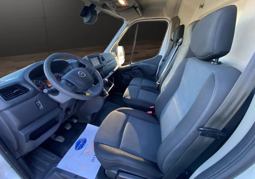 Vue intérieure côté conducteur du Nissan Interstar blanc 2022, montrant les sièges tissu et le tableau de bord avec volant.