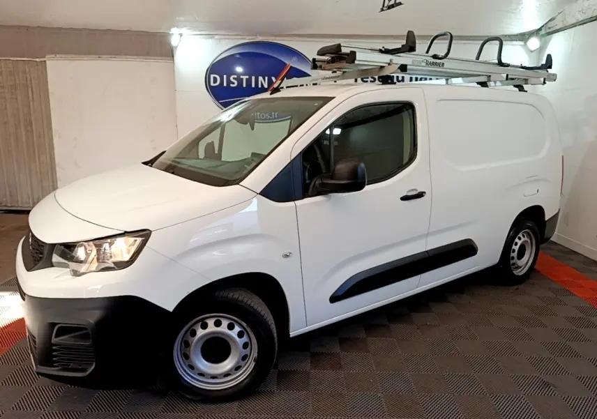 Vue 3/4 avant droite du Peugeot Partner blanc avec galerie de toit et jantes acier en intérieur fermé.