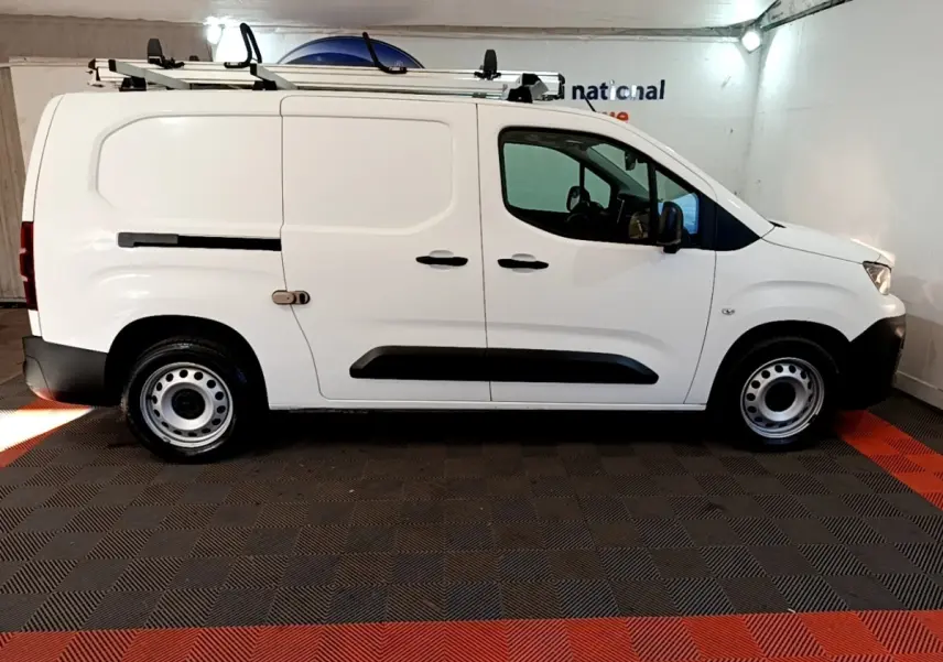 Vue latérale droite d'un utilitaire Peugeot Partner blanc avec galerie de toit et jantes acier en intérieur fermé.