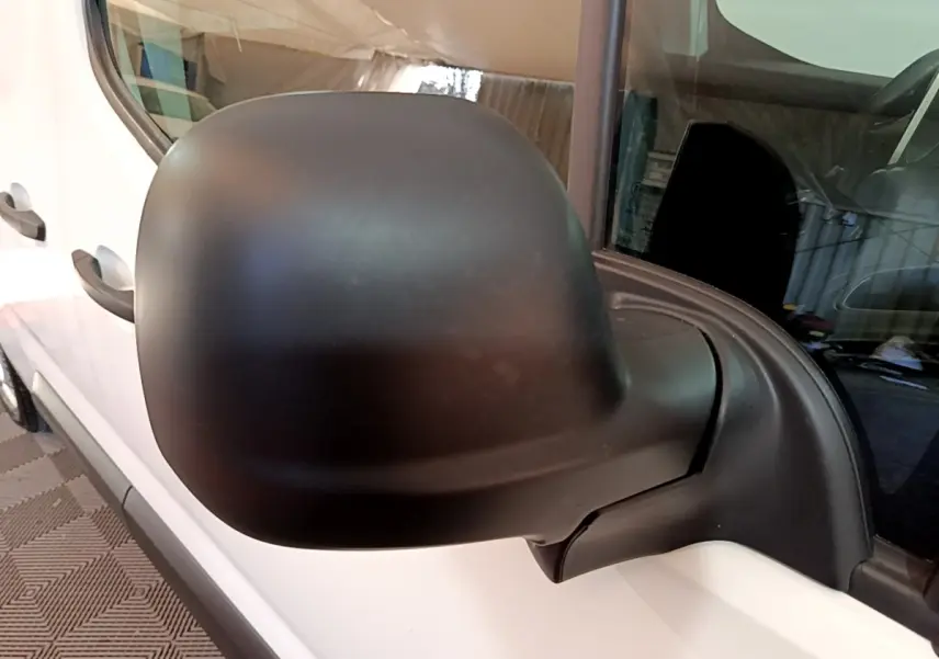 Rétroviseur noir en gros plan côté gauche d’un Peugeot Partner blanc, vue partielle du véhicule côté conducteur.