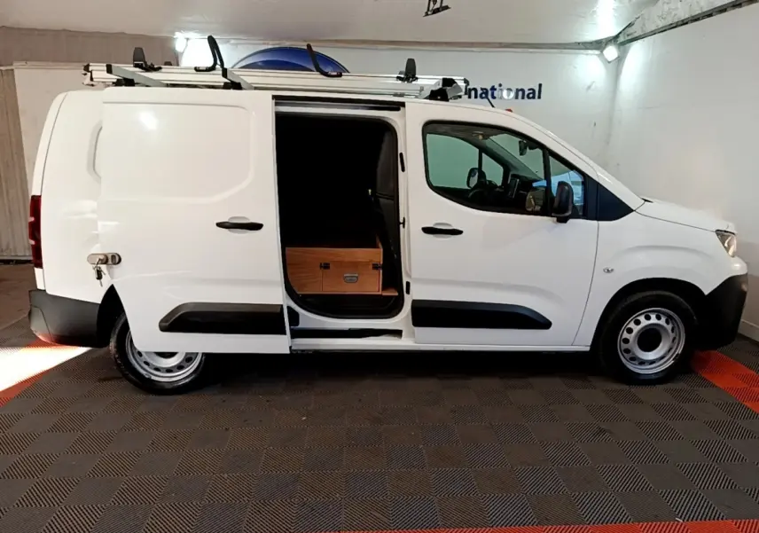Vue de profil côté droit d’un Peugeot Partner blanc avec porte coulissante ouverte et chargement visible.