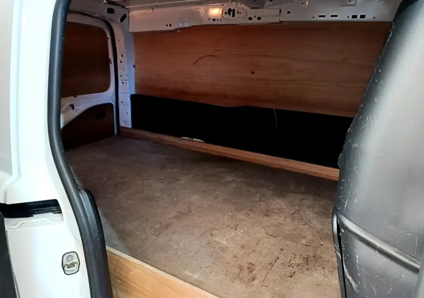 Vue intérieure du compartiment de chargement du Peugeot Partner blanc, montrant le revêtement bois et la cloison pleine arrière.