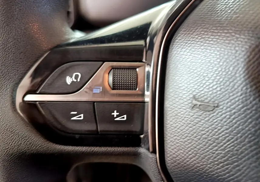 Gros plan sur les commandes de volume et de reconnaissance vocale sur le volant noir du Peugeot Partner blanc.