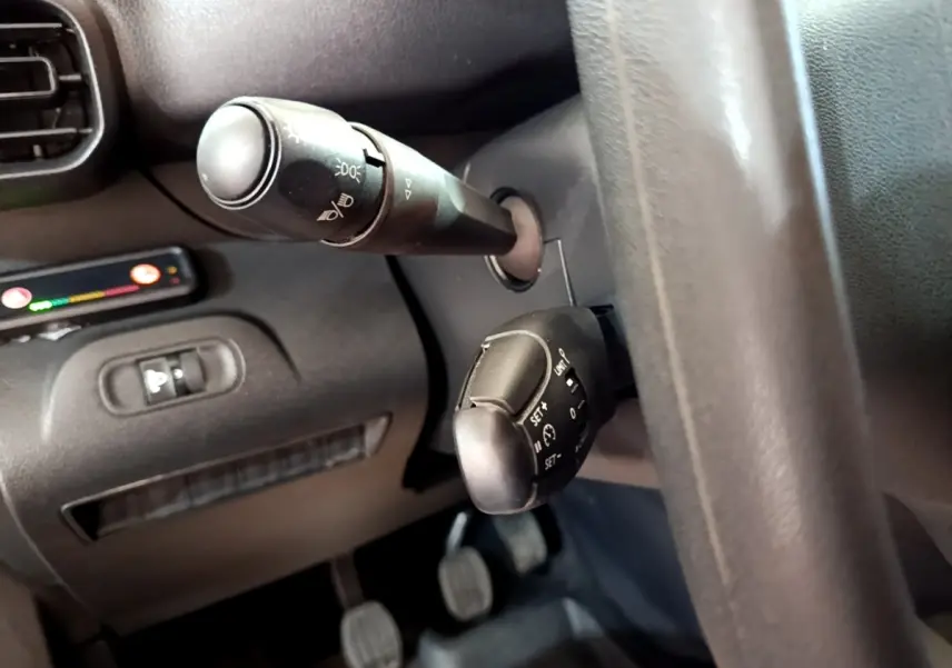 Gros plan sur les commandes au volant noir du Peugeot Partner blanc, avec levier de clignotants et régulateur de vitesse.