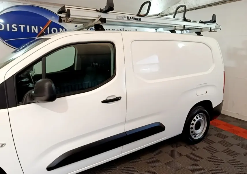 Vue latérale droite d’un Peugeot Partner blanc utilitaire avec galerie de toit et jantes acier en intérieur.
