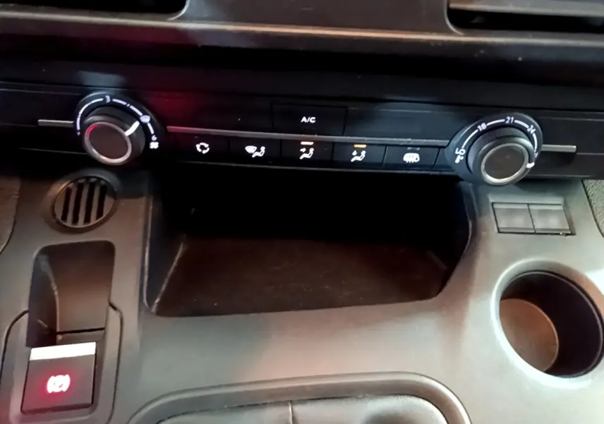 Vue rapprochée de la console centrale noire du Peugeot Partner 2021, montrant les commandes de climatisation et frein à main électrique.