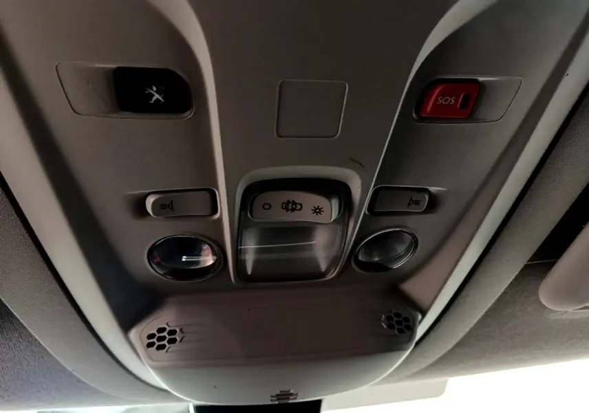 Vue intérieure en contre-plongée du plafonnier gris avec boutons d’éclairage et bouton d’appel d’urgence rouge dans un Peugeot Partner blanc.