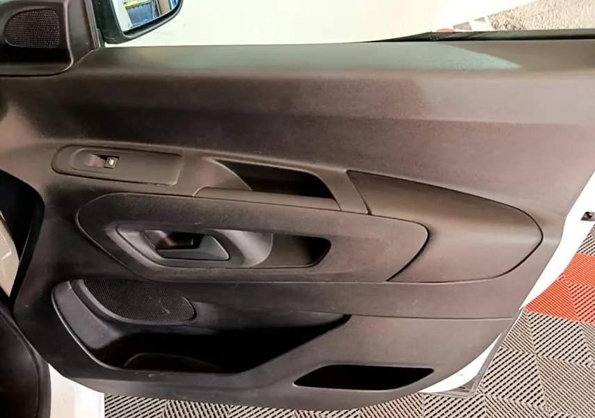 Vue rapprochée de la porte intérieure côté conducteur du Peugeot Partner blanc, avec commandes de fenêtre et rangement.