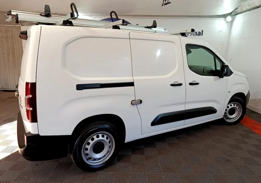 Vue côté droit d'un utilitaire Peugeot Partner blanc avec galerie de toit et jantes acier en intérieur fermé.