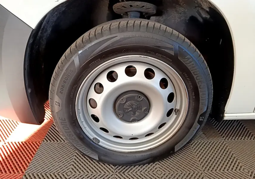 Gros plan sur la roue avant droite blanche d’un Peugeot Partner 2021 avec jante acier et logo Peugeot central.