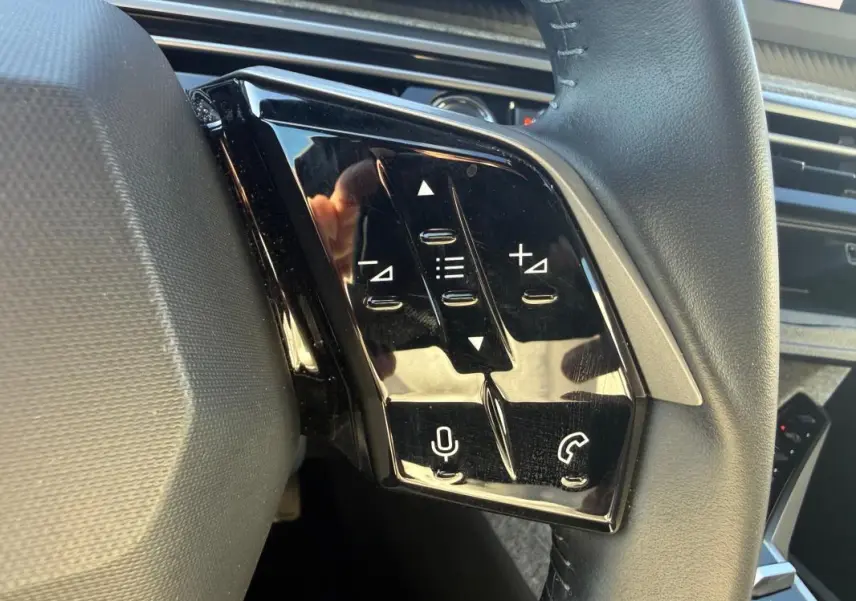 Gros plan sur les commandes tactiles noires à gauche du volant du Peugeot 3008 Hybrid gris, avec micro et téléphone.