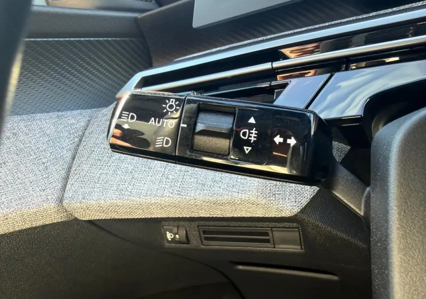 Gros plan sur la commande des feux automatique et clignotants dans l’habitacle gris du Peugeot 3008 Hybrid 145 e-DCS6 Allure.