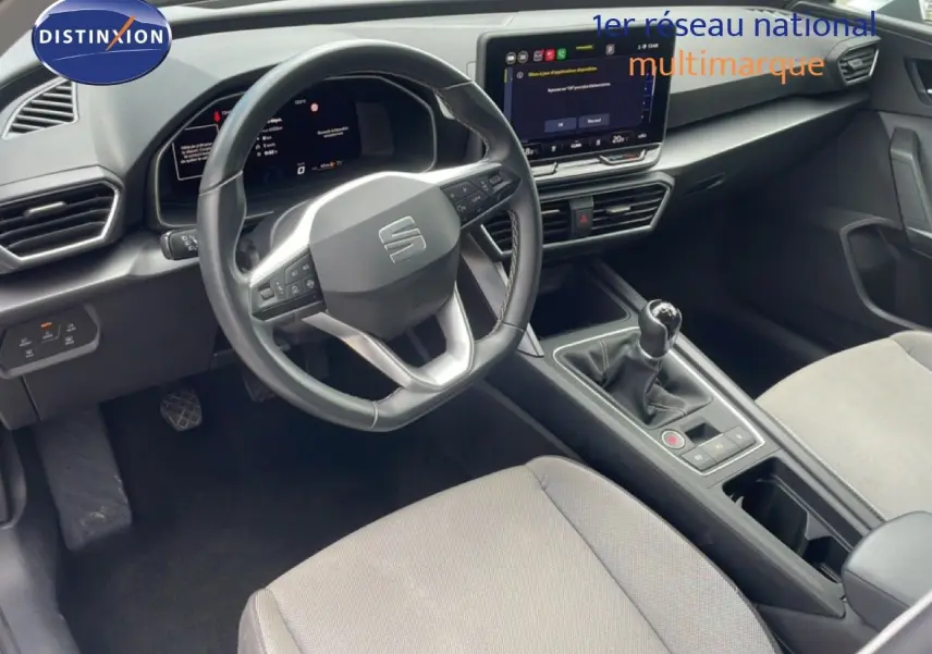 Vue intérieure de face du poste de conduite du SEAT LEON blanc neige métal, avec volant cuir multifonction et boîte manuelle.