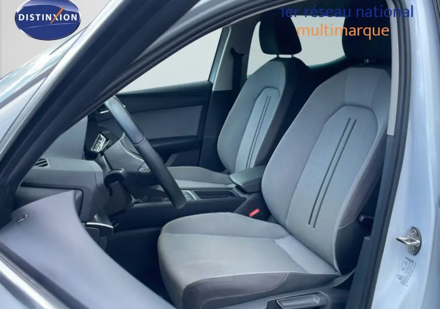 Vue intérieure côté conducteur de la SEAT LEON 2025 avec sièges tissu gris clair et volant cuir multifonction.