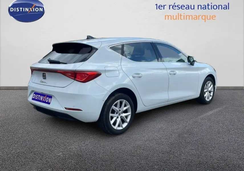 Vue 3/4 arrière droite d'une SEAT Leon blanc neige métal avec feux arrière allongés et jantes alliage.