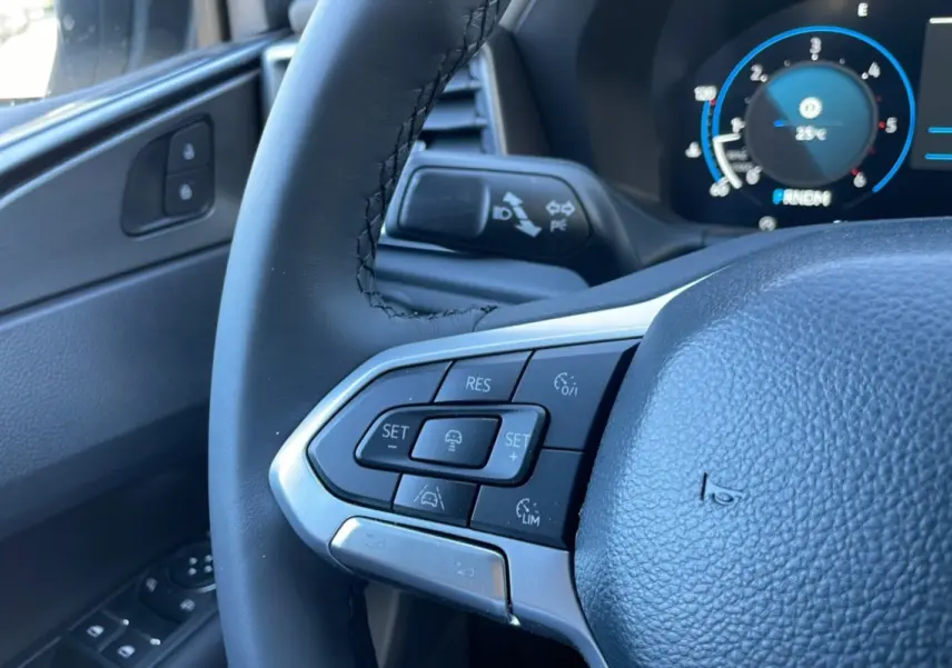 Gros plan sur le volant cuir multifonctions côté gauche du Volkswagen Amarok blanc, avec commandes de régulateur et tableau de bord digital.