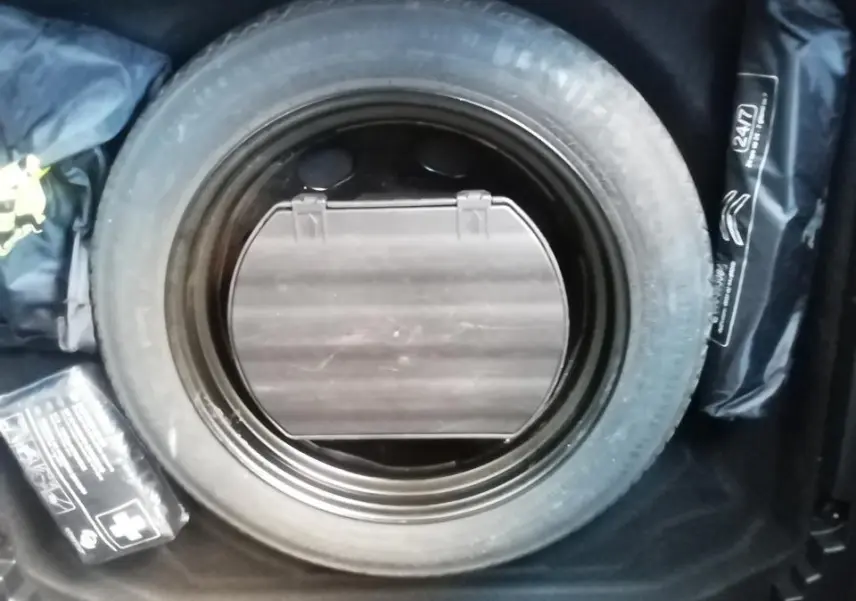 Vue en plongée sur la roue de secours et accessoires dans le coffre d'une Citroën C5 Aircross gris.