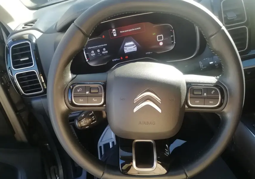 Vue rapprochée du volant noir du Citroën C5 Aircross avec tableau de bord numérique affichant une porte ouverte.