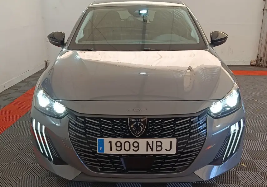 Vue frontale d'une Peugeot 208 gris foncé avec phares LED allumés et calandre noire distinctive.