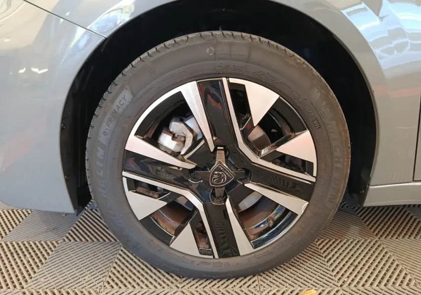 Gros plan sur la roue avant gauche gris foncé d'une Peugeot 208 PureTech 100 S&S Allure avec jante noire et argentée.