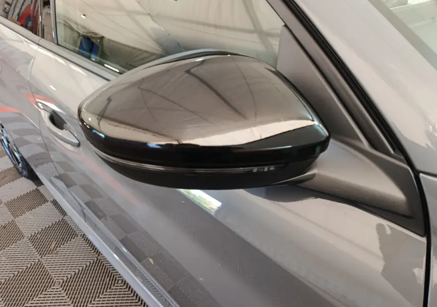 Rétroviseur noir côté gauche d'une Peugeot 208 gris foncé, vue rapprochée sur la portière avant.