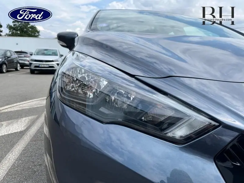 Gros plan sur le phare avant droit d'une Nissan Micra gris acier, mettant en valeur le design moderne du bloc optique.